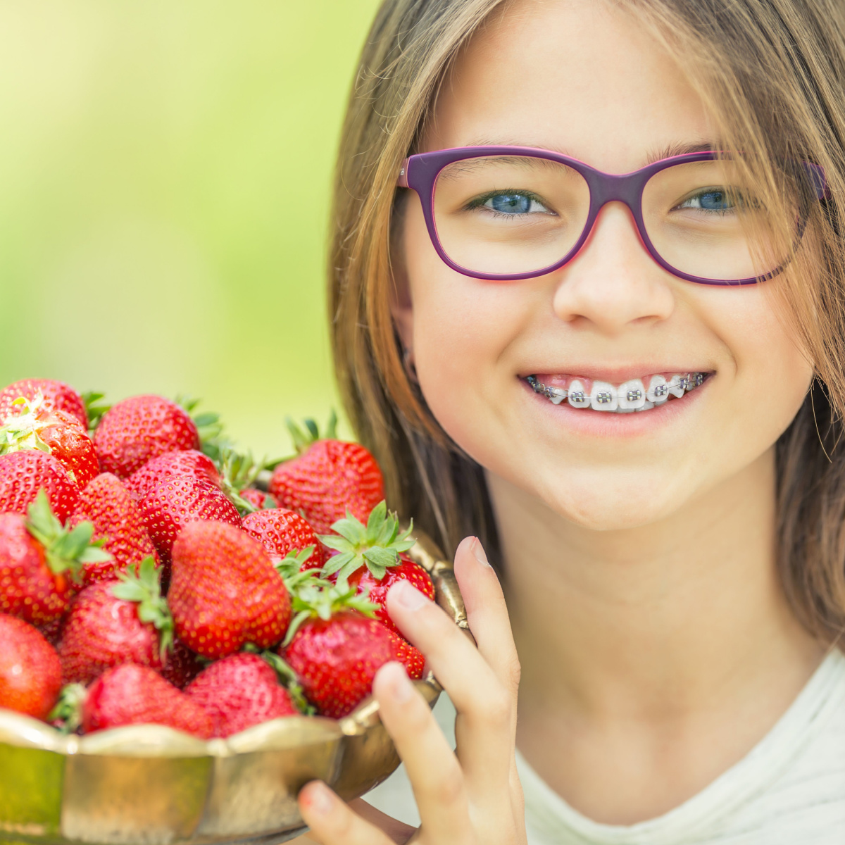 Girl holds up a basket of strawberries she can easily eat even with her South Houston dental braces.