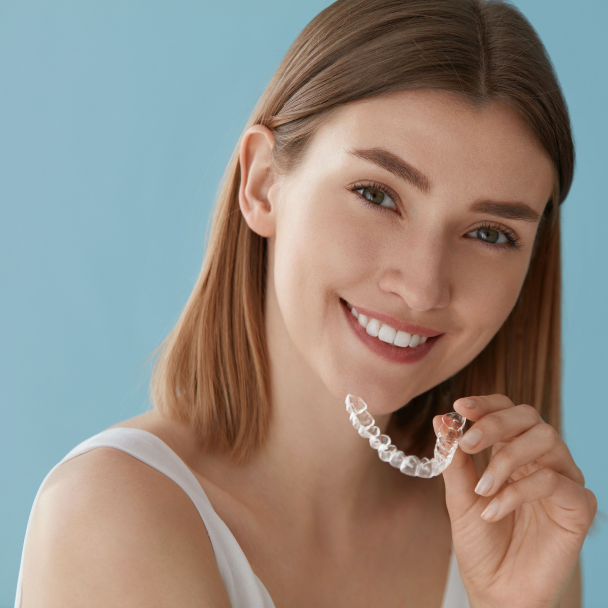 Woman with a straight smile holds her Houston clear aligners.