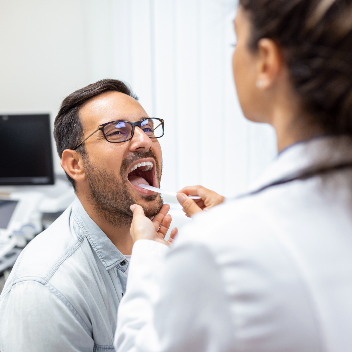 doctor using inspection spatula to examine patient's throat