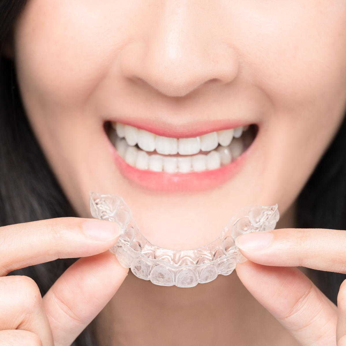 Asian woman holds a Houston Invisalign and smiles.